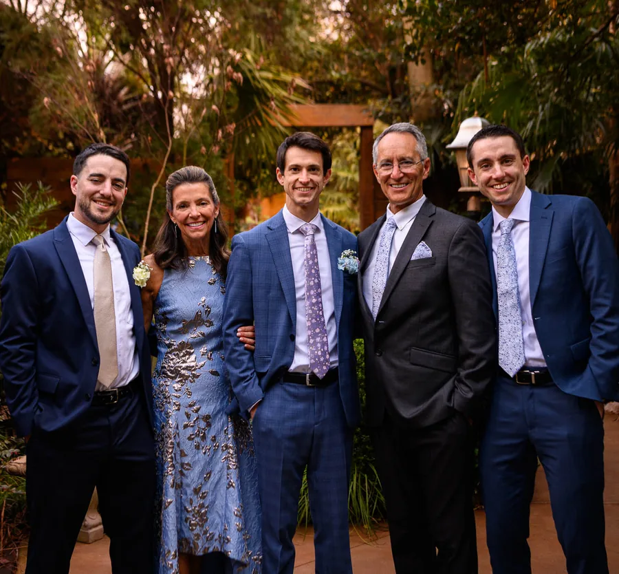 Jeff with his parents and two brothers, all in suits, smiling together among garden greenery at a family wedding.